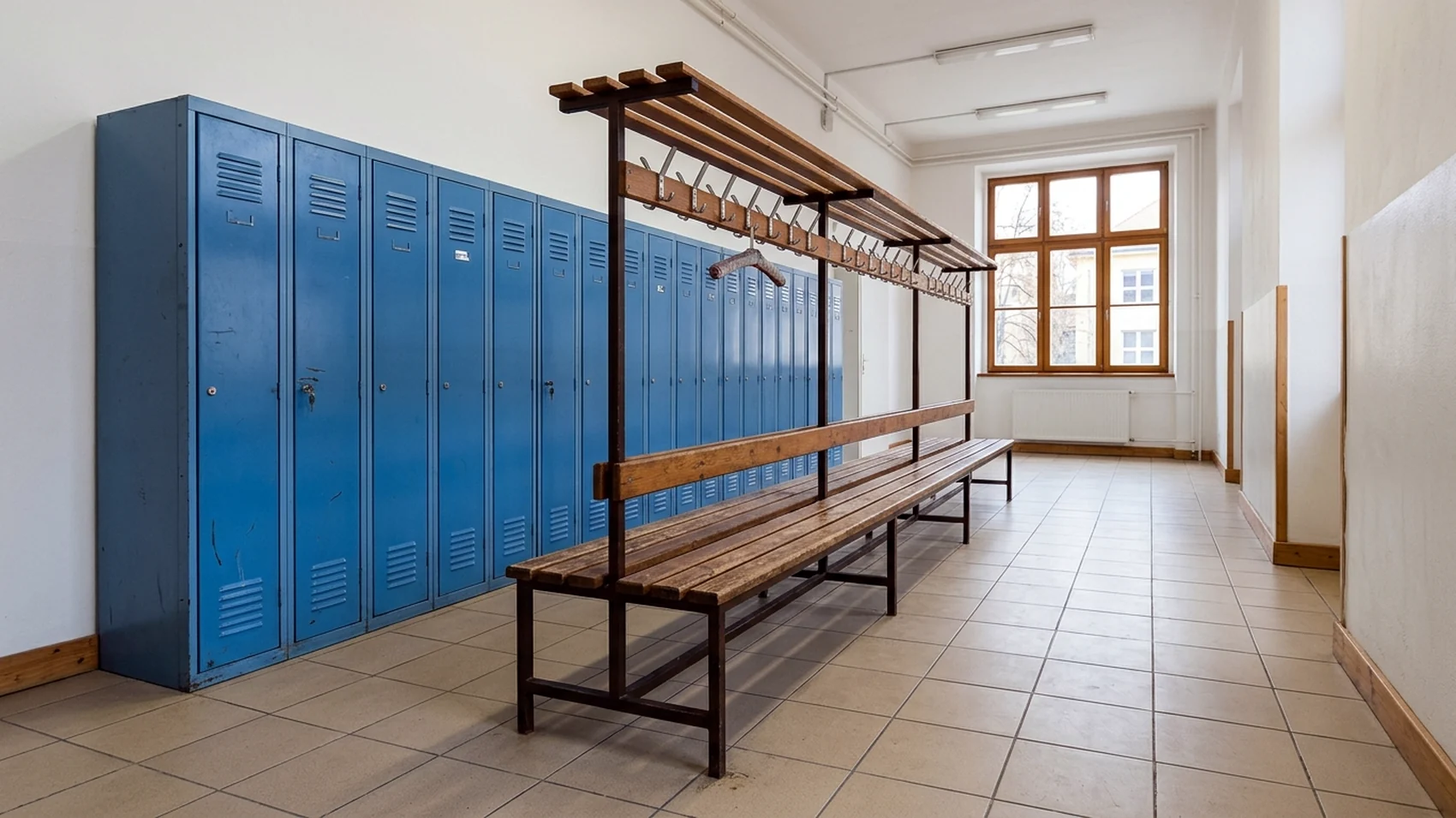 Školní šatna s modrými skříňkami a lavičkou s věšáky